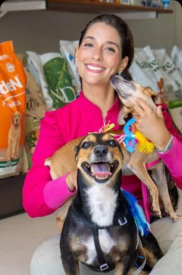 Atendente da Pet Seguro sorrindo, sentada na loja com dois cachorros no colo